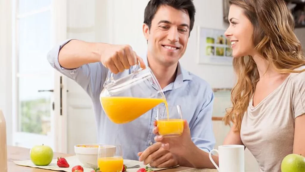 Hombre sirviendo un jugo de naranja a su esposa