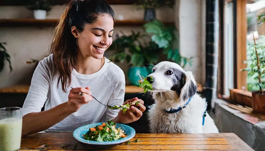 Mujer comiendo vegetales junto a su perro